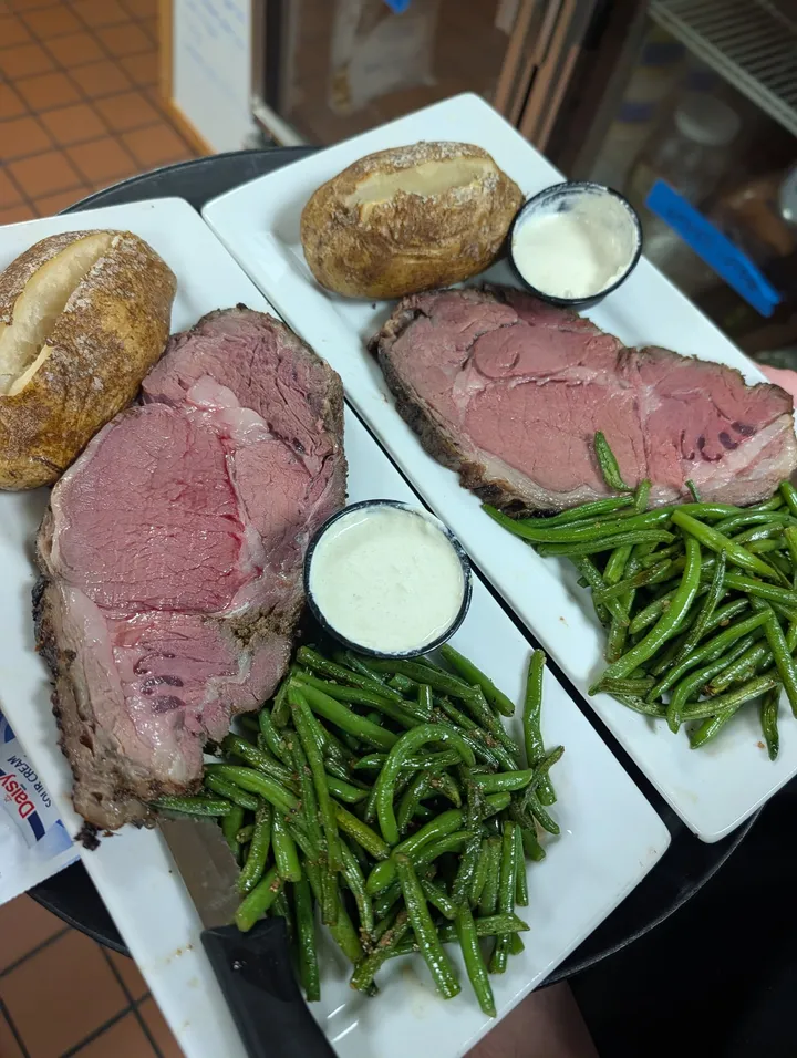 Two prime rib plates with baked potatoes, green beans and creamy dipping sauce